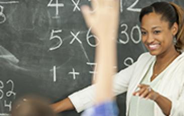 Image of teacher at chalkboard smiling at student raising hand