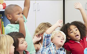 elementary children raising their hands excitedly