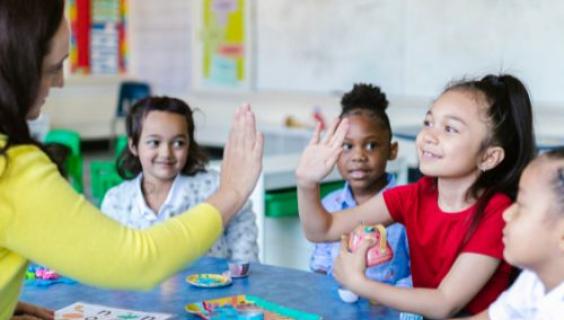 a teacher with four elementary students giving high-fives