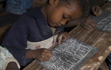 African boy writing with chalk on slate